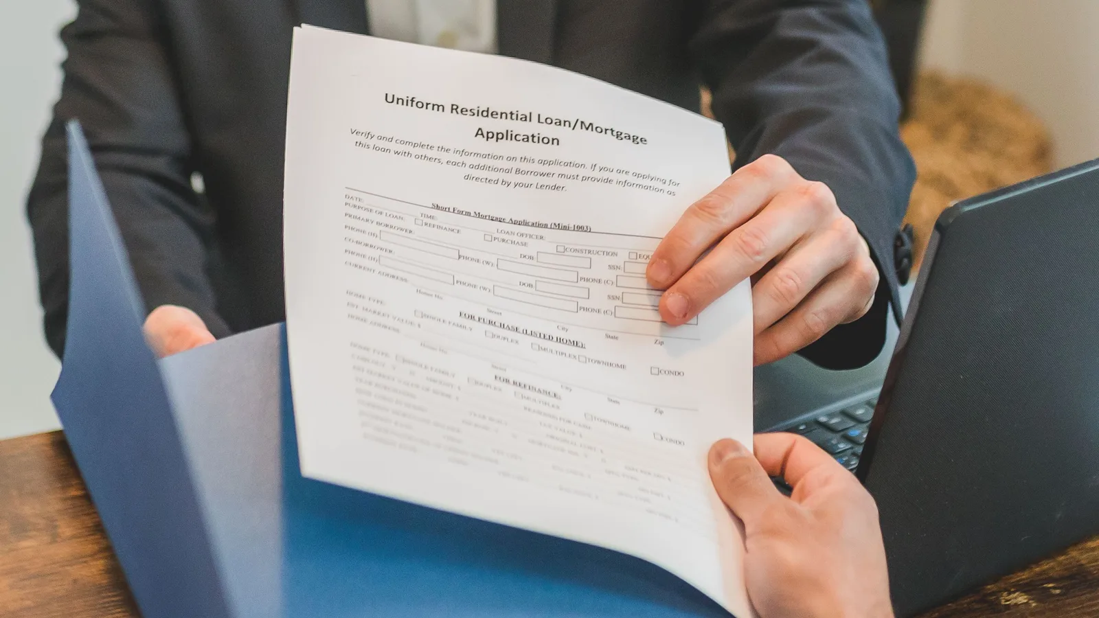 Hands exchanging a signed mortgage application document across a desk