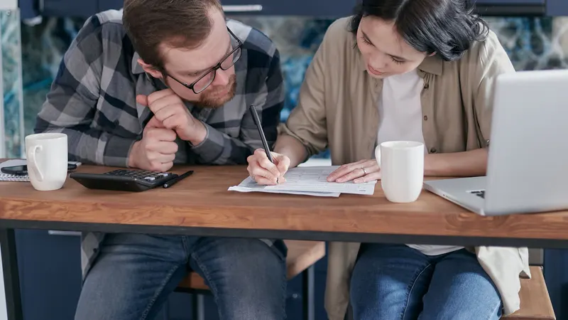 Couple sitting at their kitchen table with a calculator and paperwork, working out how much they can borrow for a home loan