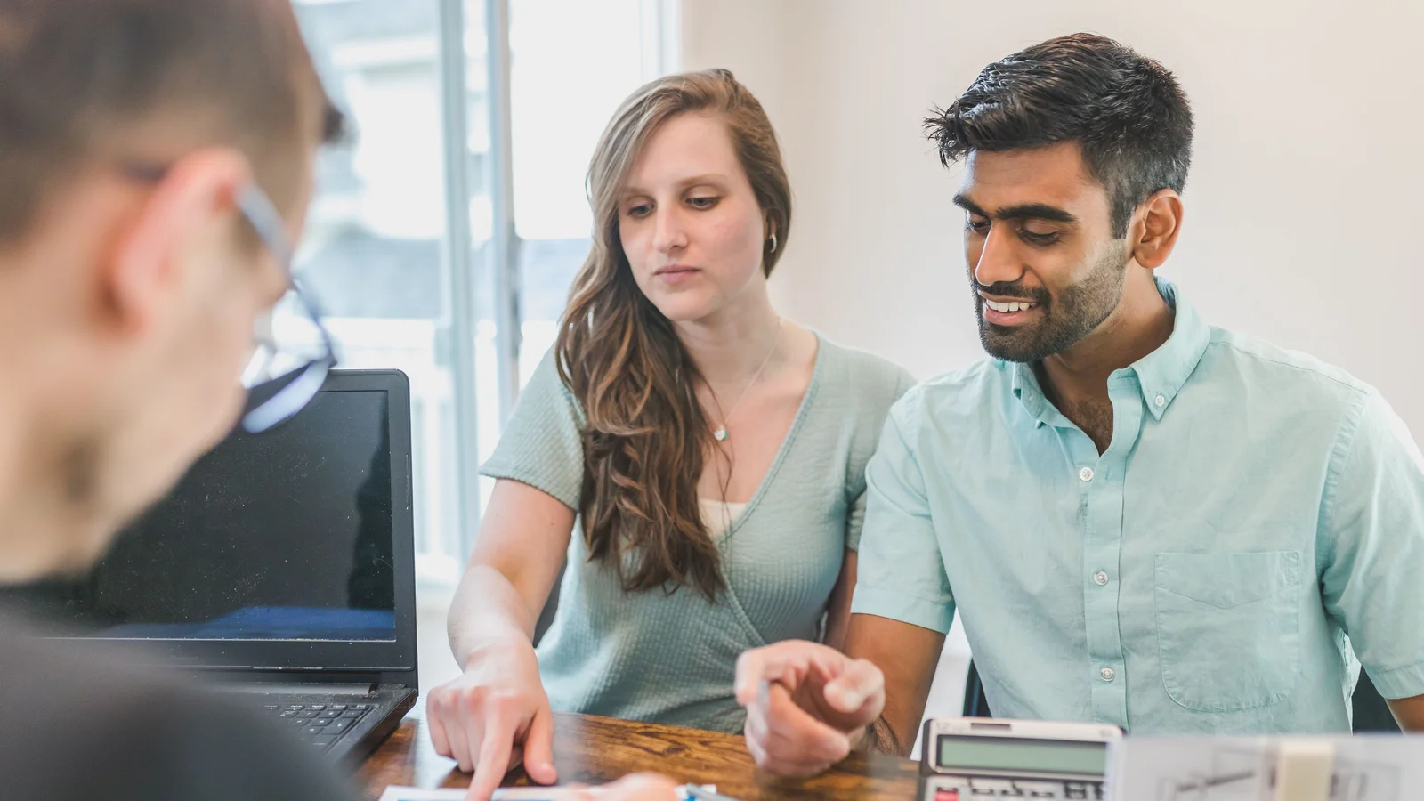 Couple sitting at table with a calculator reviewing mortgage figures with an adviser