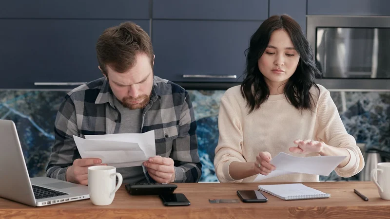 Couple sitting together at kitchen counter reviewing online banking and home loan budget on laptop